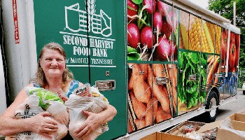 woman holding bags of groceries standing in front of a Second Harvest trailer