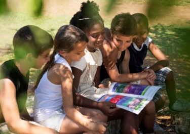 five children sitting closely together reading a book
