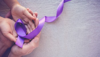 Adult hands holding child's hands with purple ribbon