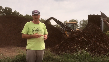 Commercial composting employee standing in front of compost pile and machinery