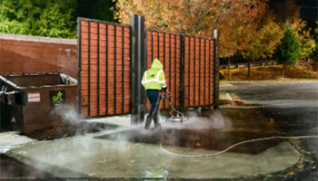 Employee cleaning drive in front of dumpster
