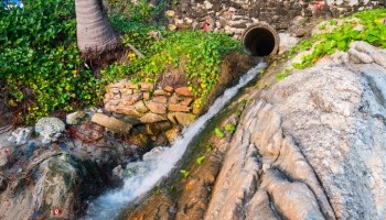 a small waterfall flowing down a rocky hillside from a water drain