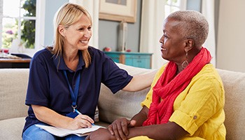 two women sitting on a couch talking, one writing on paper and smiling