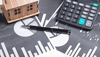 calculator, pen, and house model on top of charts and graphs