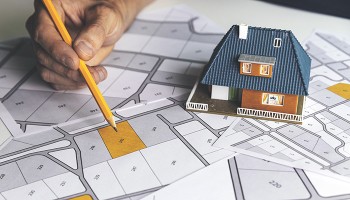 Hand holding pencil with neighborhood plans and a small house model