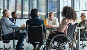 Photo: group of people sitting around a table including one person in wheelchair