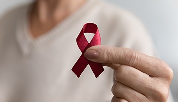 photo: person holding red ribbon repesenting HIV awareness
