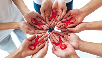photo: hands of multiple people holding red ribbons representing HIV awareness