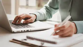 person using laptop and writing in a notebook