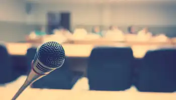 Microphone in focus with blurred auditorium seating and stage lights in background.