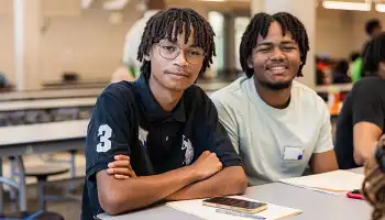 Two boys sitting at a table in cafeteria looking at the camera
