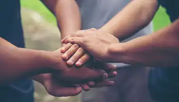 Four hands stacked together in a team unity gesture outdoors.