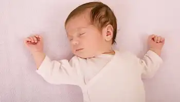 Sleeping newborn baby in cream-colored clothing on pink bedding.