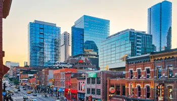 Urban skyline at sunset with modern blue glass skyscrapers rising above historic brick buildings.