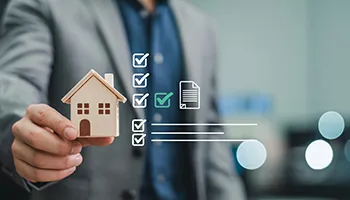 Person holding house model with property checklist icons displayed.