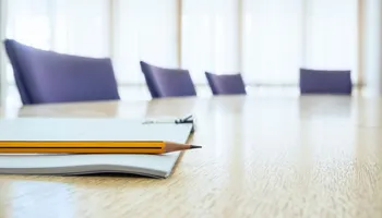 Notepad on wooden table with blurred office chairs in background.