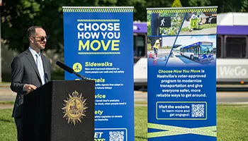 Mayor Freddie O'Connell standing next to blue "Choose Your Move" promotional signs outdoors.