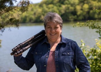 Photographer Robin Conover posing in front of a scenic lake