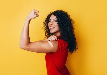 Woman holding up arm in strength gesture showing off band-aid on shoulder