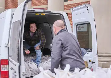 photo of two men loading bagged groceries into the back of a van.