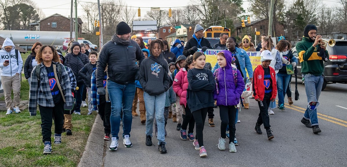 group of children and adults walking on a street in a parade