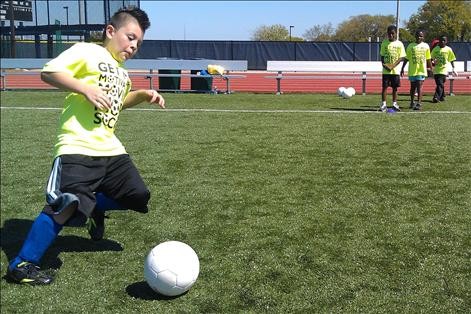 Photo of youth kicking soccer ball while three teammates look on.
