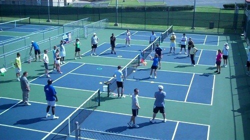 Photo of several adults playing tennis on a multi-court facility