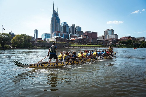 photo of dragon boat being rowed on the Cumberland River with the Nashville skyline in the background