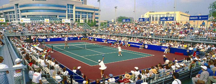 Photo of a tennis match on an outdoor court with several spectators watching