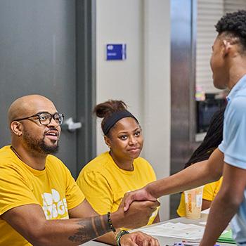Two volunteers greeting a young person at an event
