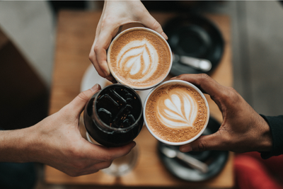 Three hands holding three coffee cups with latte art, viewed from above.