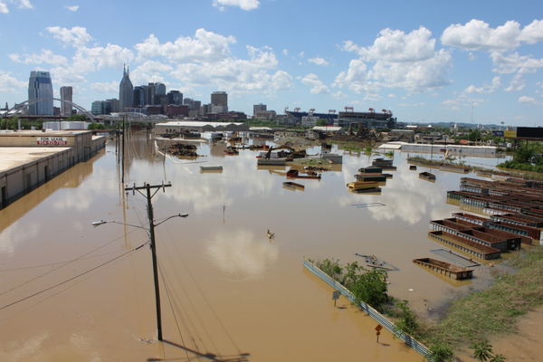 Flooded industrial area with submerged vehicles and buildings under blue sky with clouds.