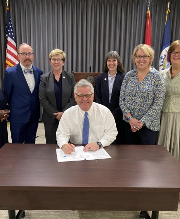 Mayor John Cooper sitting at desk with Metro Council members standing behind