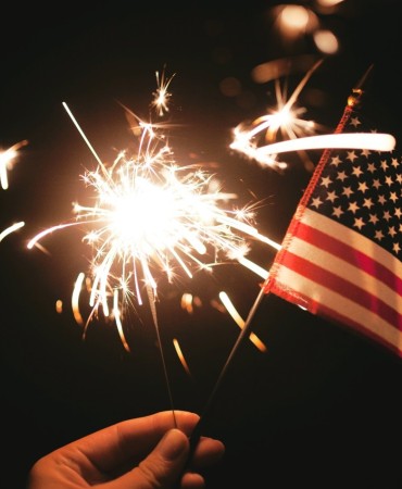 Fireworks in sky behind handheld USA flag in the dark