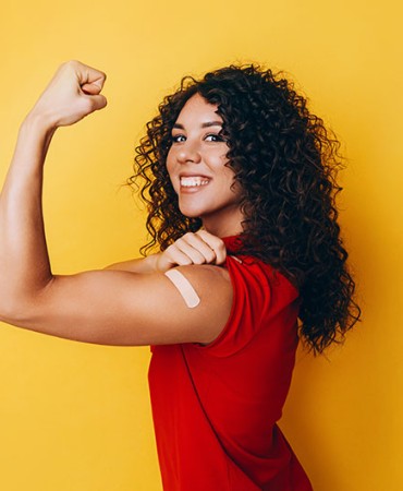Woman holding up arm in strength gesture showing off band-aid on shoulder