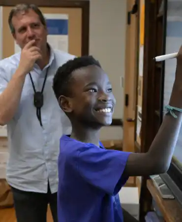 student writing on digital whiteboard while teacher looks on