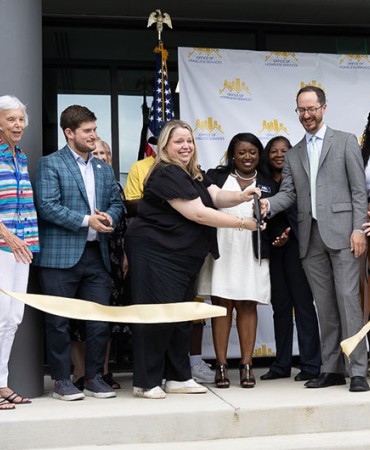 ribbon cutting ceremony at the Strobel House grand opening ceremony with several people on stage including Mayor Freddie O'Connell