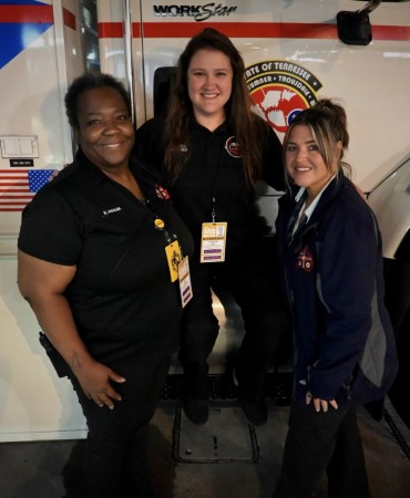 3 woman stand in front of mobile command vehicle