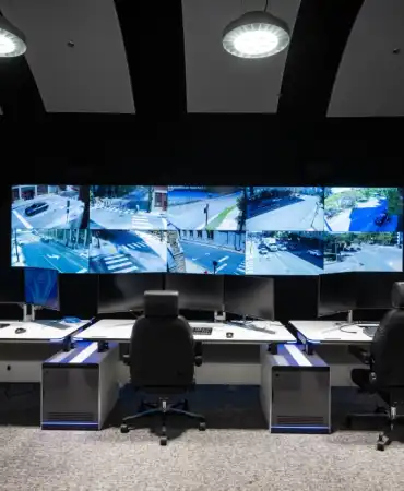 Interior view of the Traffic Management Center showing multiple large monitors displaying traffic camera feeds with workstations for staff to monitor traffic conditions