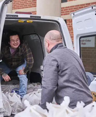 photo of two men loading bagged groceries into the back of a van.