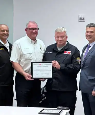 Four men in uniforms and business attire holding a certificate during an official presentation ceremony.