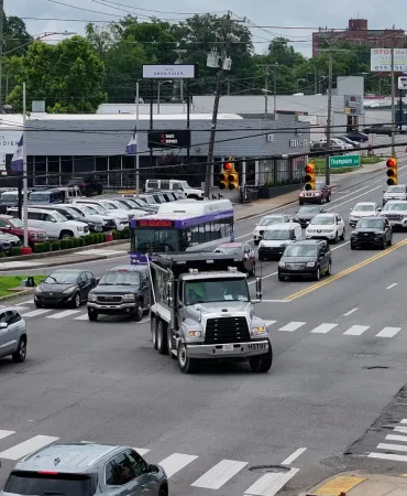 Busy suburban shopping center parking lot with multiple vehicles and commercial buildings under cloudy sky.