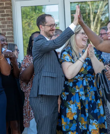 Group of people in formal attire clapping and celebrating at an outdoor event.