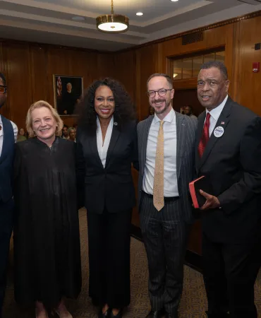 Seven professionals in business attire standing together in a formal indoor setting.