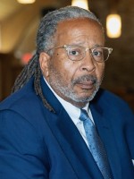 Image of Davie Tucker, African-American man with long locs and glasses, with a blue suit and tie, 