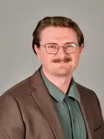 Headshot of Gavin Crowell-Williamson, pictured in a green shirt and brown suit