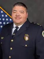 Officer in dress uniform with American flag in background, official portrait photograph.