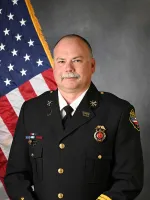 Fire chief in dress uniform standing in front of American flag.