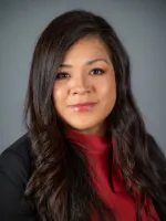 Woman with long dark hair wearing a red top against a gray background, professional headshot.