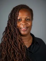 Woman with long braids smiling at camera against gray background.